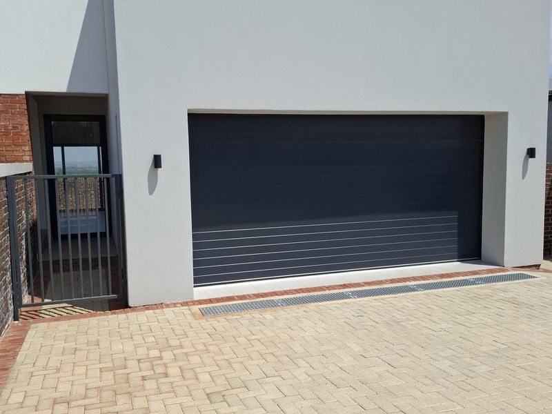 Modern front facade featuring a clean white finish, a dark sectional garage door, paved driveway, and a secure side pedestrian gate.