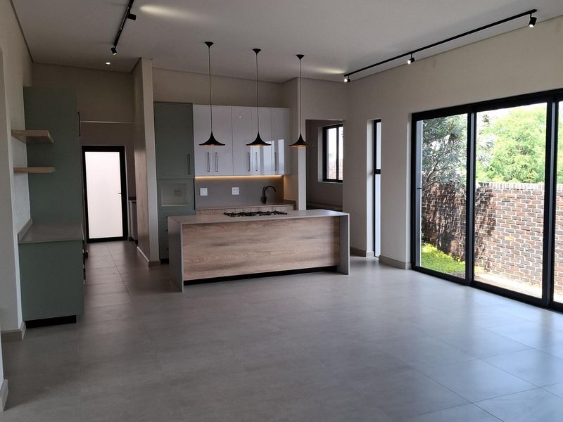 Modern open-plan kitchen featuring a central island with integrated hob, sleek cabinetry, and large sliding glass doors opening to the rear garden.