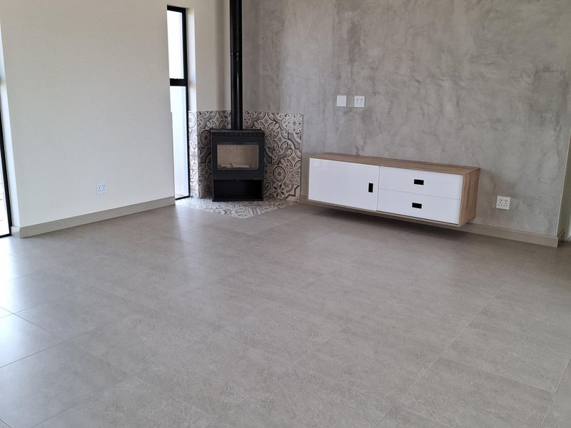 Modern living area featuring large format floor tiles, a feature concrete wall, a built-in fireplace, and a wall-mounted air conditioning unit.