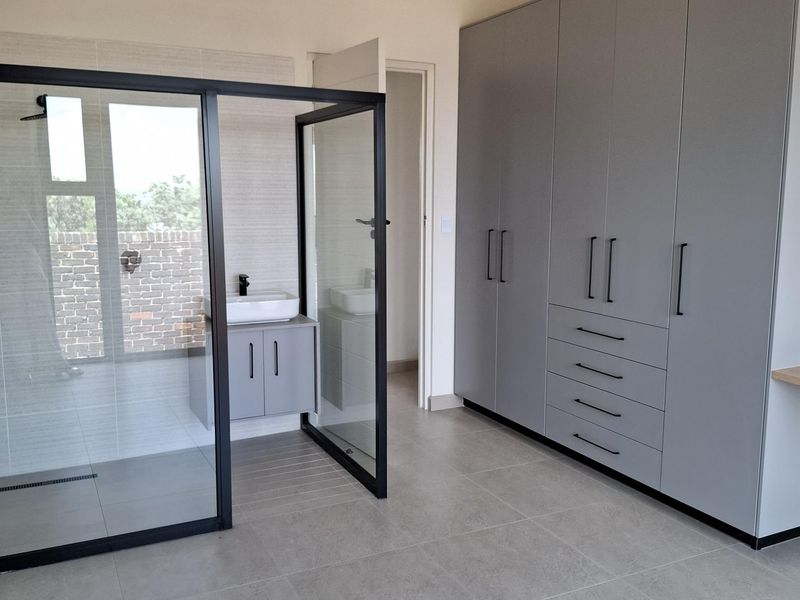 Modern bedroom featuring a large built-in wardrobe and an integrated glass-enclosed en-suite bathroom with a vanity and shower.