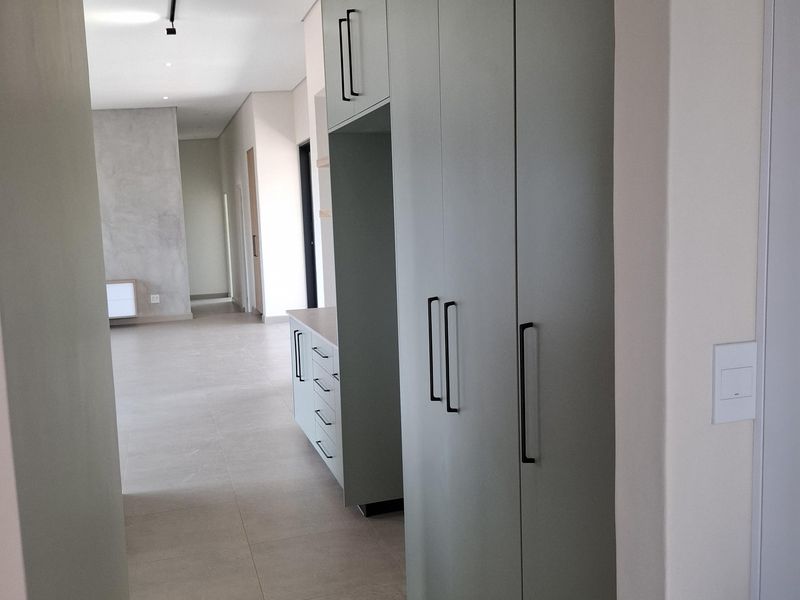 A modern hallway featuring floor-to-ceiling sage green cabinetry with matte black hardware, leading into an open-plan living area with neutral tiled flooring.