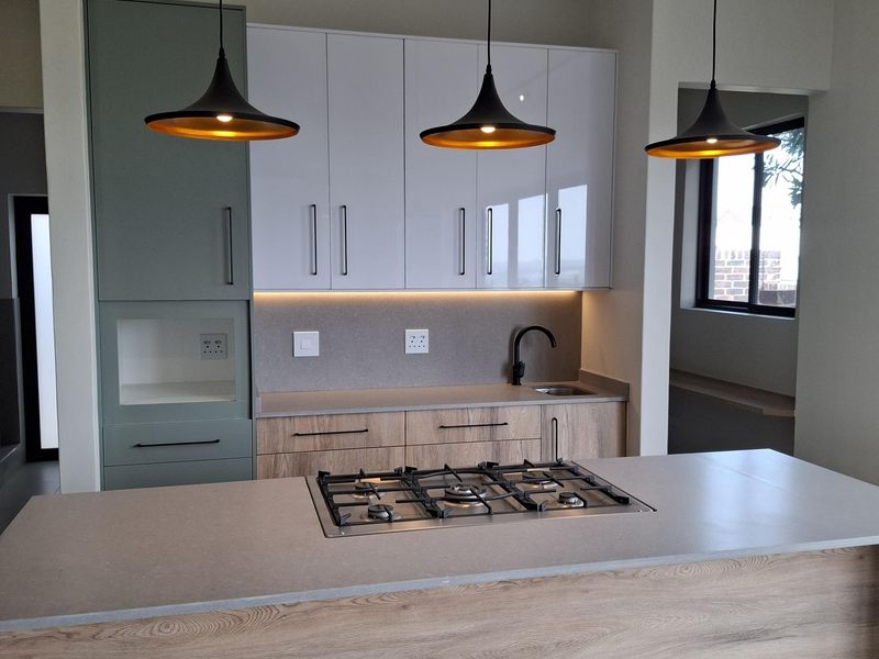 Modern kitchen featuring a central island with a built-in gas hob, sleek cabinetry, stone countertops, and contemporary pendant lighting.