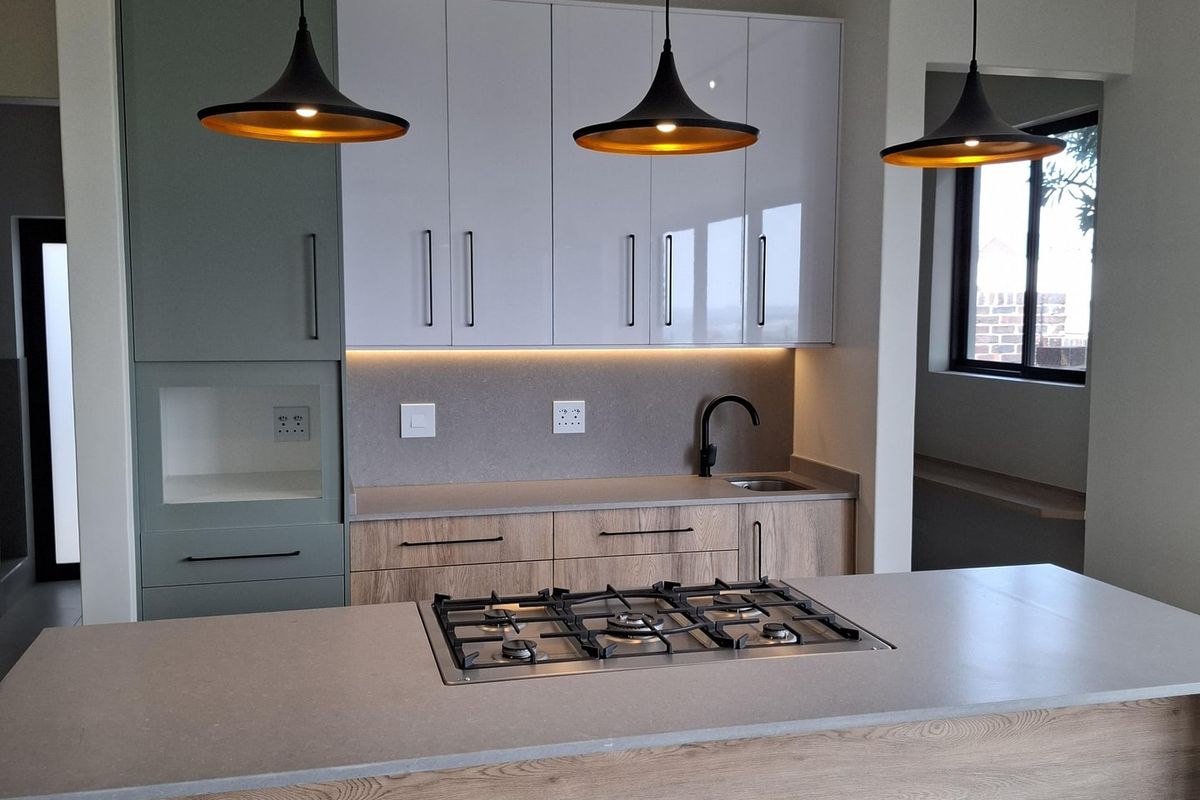 Modern kitchen featuring a central island with a built-in gas hob, sleek cabinetry, stone countertops, and contemporary pendant lighting.