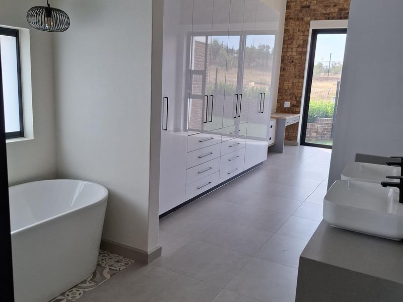 Modern bathroom featuring a freestanding bathtub, dual vessel sinks on a floating vanity, extensive built-in cabinetry, and a feature brick wall.