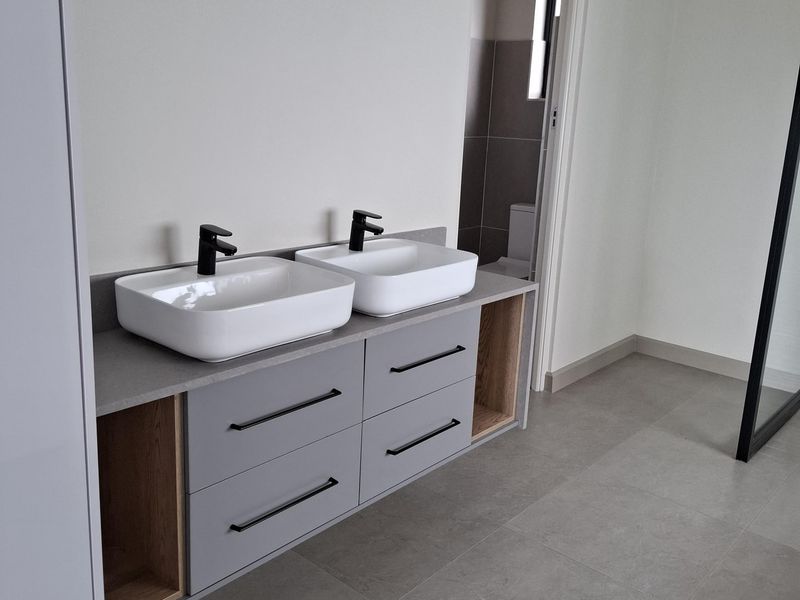 Modern bathroom featuring a floating double vanity with grey cabinetry, stone countertop, and contemporary black basin mixers.