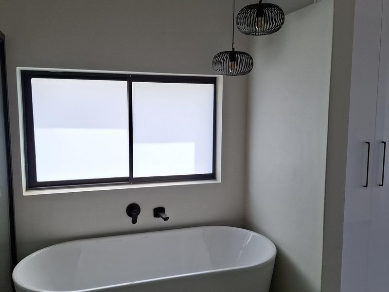 Modern bathroom featuring a freestanding bathtub, wall-mounted matte black tapware, patterned floor tiles, and built-in cabinetry.