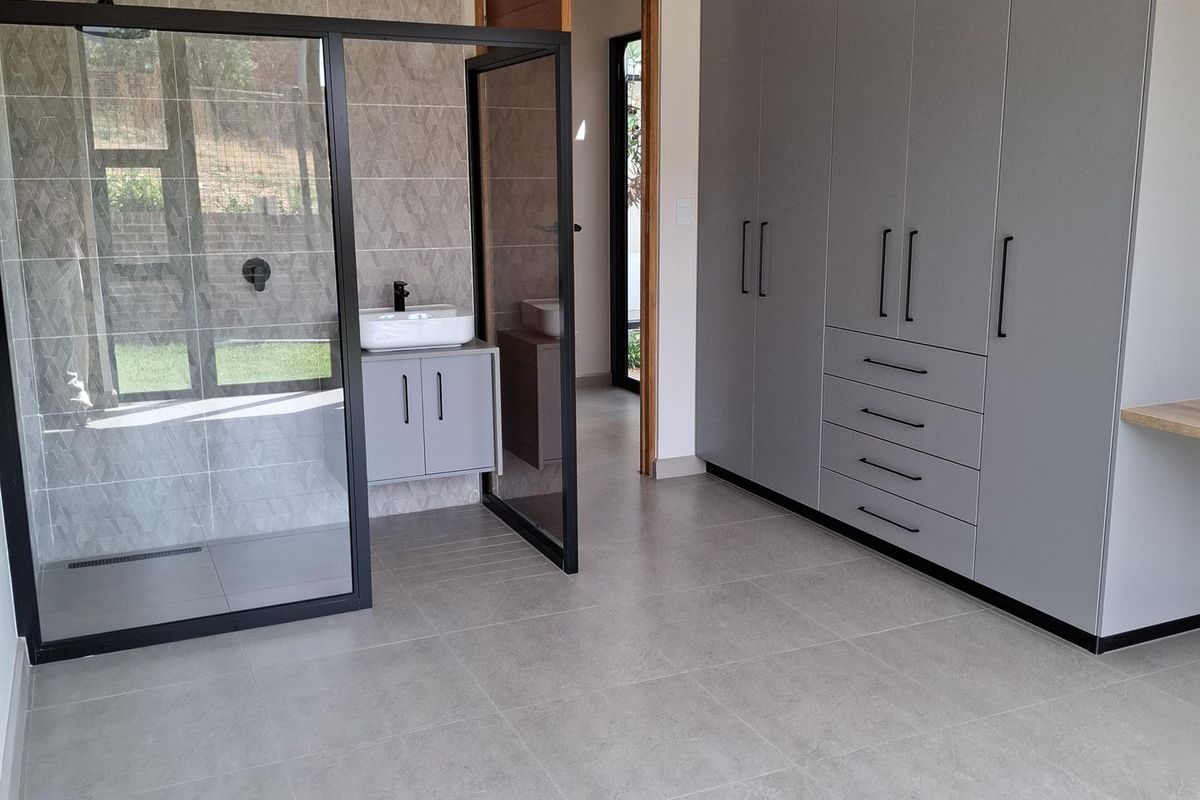 Modern bedroom featuring extensive built-in grey cabinetry and an open-plan en-suite bathroom with a walk-in shower and vanity.