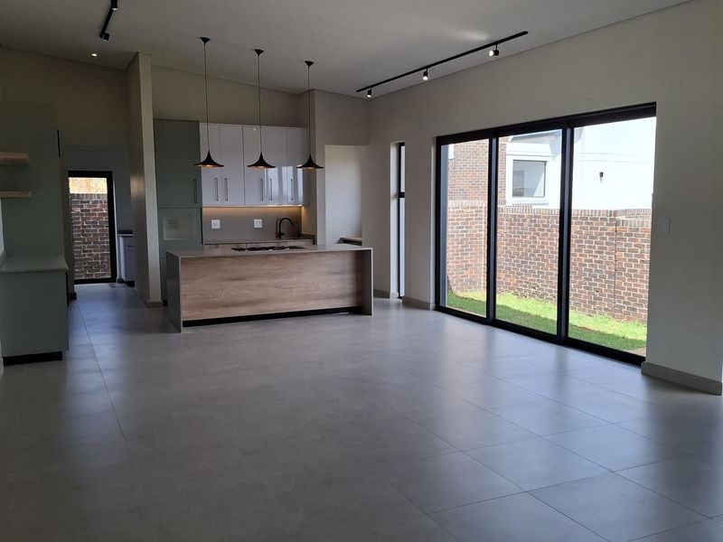 Spacious open-plan living and kitchen area featuring modern cabinetry, a central island, sleek track lighting, and large sliding doors opening to the rear garden.