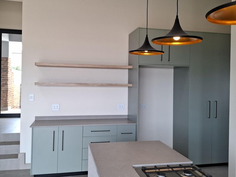 Modern kitchen featuring sage green cabinetry, stone countertops, a built-in gas cooktop, floating timber shelves, and contemporary pendant lighting.