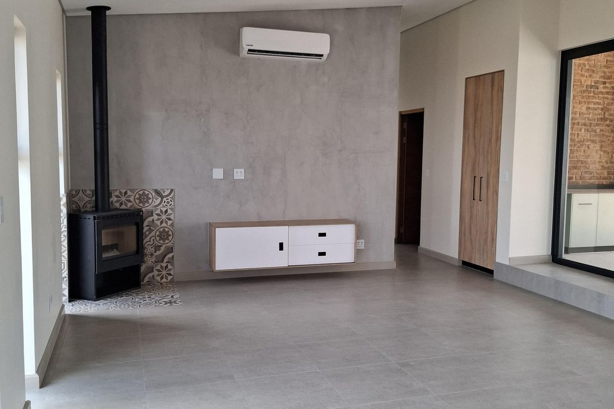 Spacious living area featuring large format floor tiles, a modern freestanding fireplace with decorative tiling, and a wall-mounted air conditioning unit.