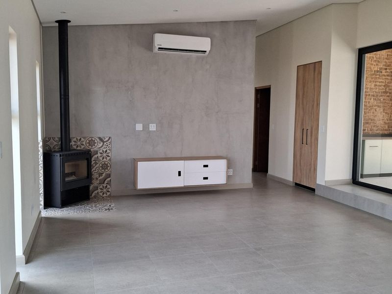 Spacious living area featuring large format floor tiles, a modern freestanding fireplace with decorative tiling, and a wall-mounted air conditioning unit.
