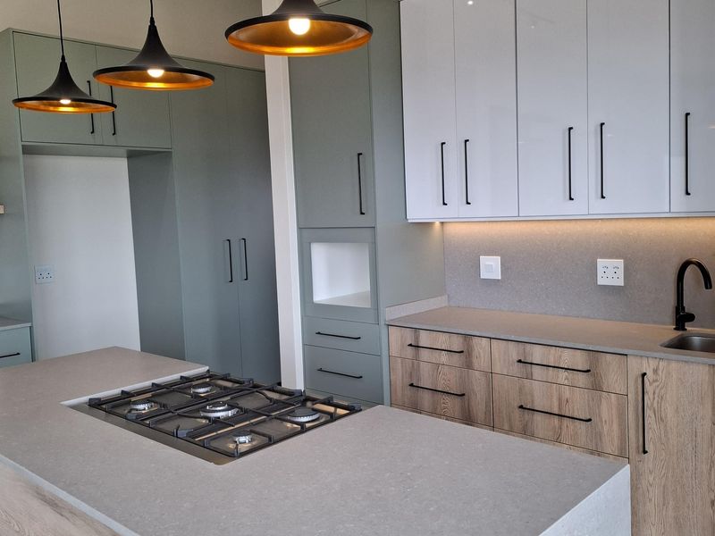 Modern kitchen featuring a central island with a gas hob, two-tone cabinetry, stone countertops, and contemporary pendant lighting.