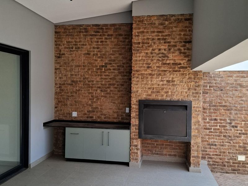 Covered patio area featuring an exposed brick wall, built-in braai, and modern cabinetry, providing an ideal space for outdoor entertaining.