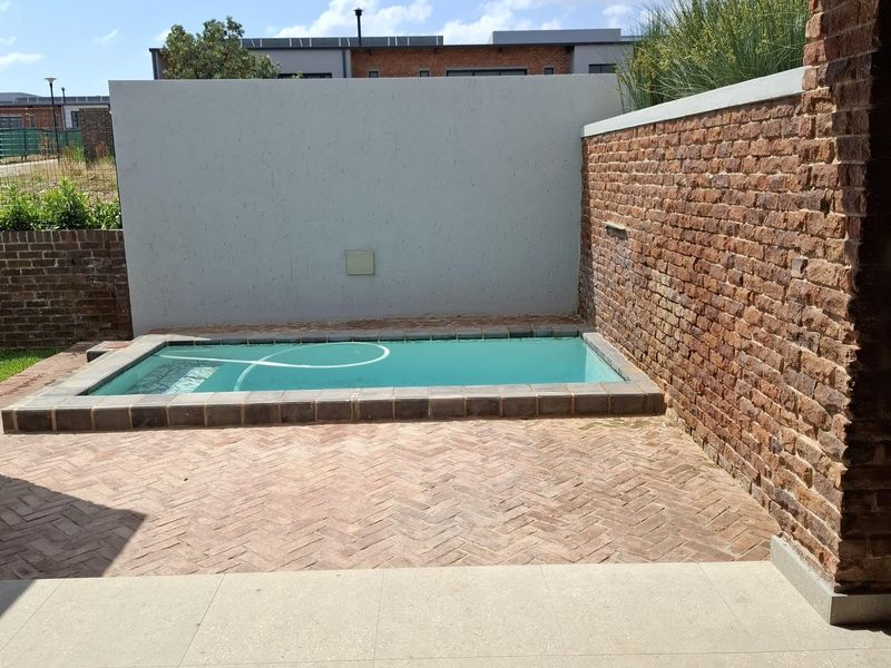 A private plunge pool area featuring herringbone brick paving, an exposed brick feature wall, and a covered tiled patio space.