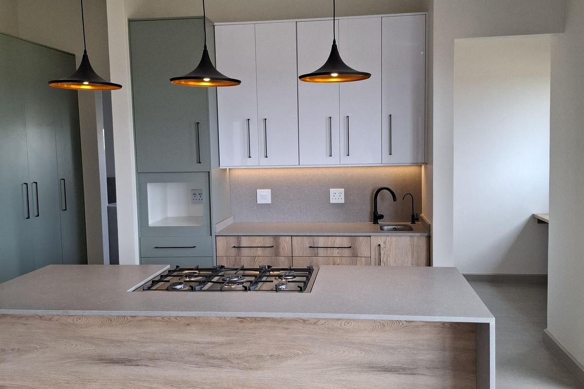Modern kitchen featuring a central island with a built-in gas hob, sleek two-tone cabinetry, and contemporary pendant lighting in a clean, minimalist space.