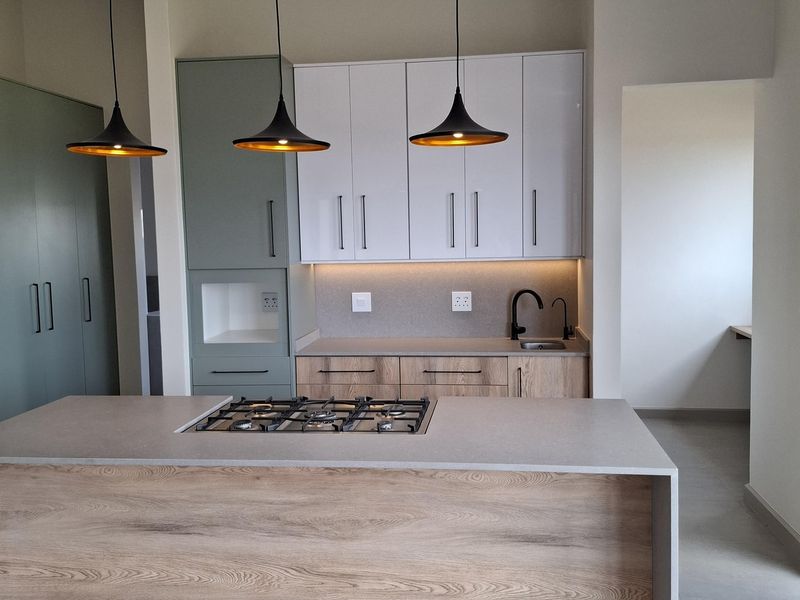 Modern kitchen featuring a central island with a built-in gas hob, sleek two-tone cabinetry, and contemporary pendant lighting in a clean, minimalist space.