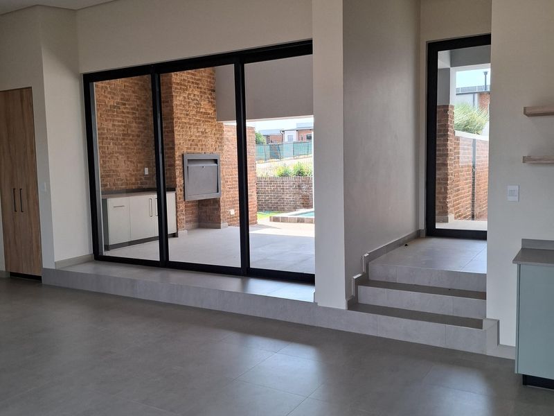 Spacious open-plan living area featuring large sliding doors leading to an outdoor patio with a built-in braai and modern tiled finishes.