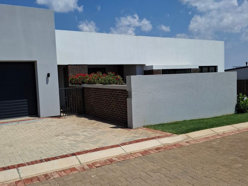 Modern contemporary house exterior featuring a clean plastered facade, brick boundary wall, paved driveway, and a secure garage entrance.