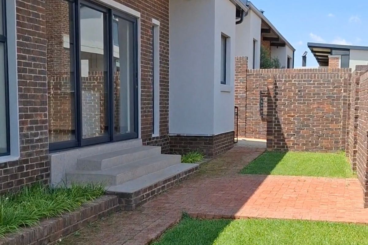 Rear exterior view featuring a modern brick facade, sliding glass doors, concrete steps, and a well-maintained garden with brick paving.