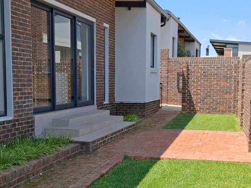 Rear exterior view featuring a modern brick facade, sliding glass doors, concrete steps, and a well-maintained garden with brick paving.