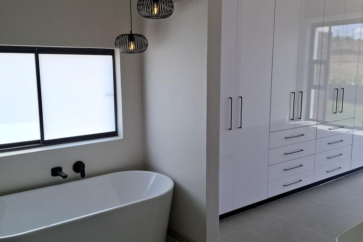 Modern bathroom featuring a sleek freestanding bathtub, wall-mounted fixtures, and extensive built-in white cabinetry with integrated storage.
