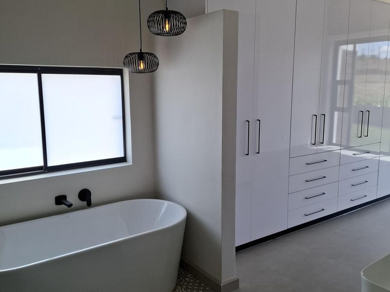 Modern bathroom featuring a sleek freestanding bathtub, wall-mounted fixtures, and extensive built-in white cabinetry with integrated storage.