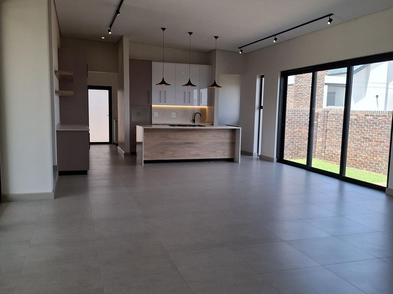 Spacious open-plan living and kitchen area featuring modern cabinetry, a central island, large sliding glass doors, and neutral tiled flooring throughout.