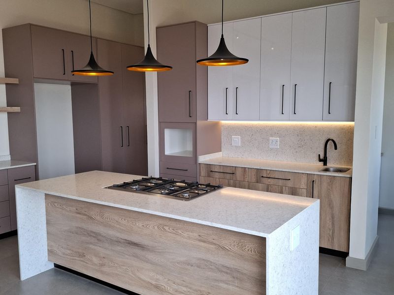 Modern kitchen featuring a central island with a gas hob, stone countertops, two-tone cabinetry, and integrated under-cabinet lighting.