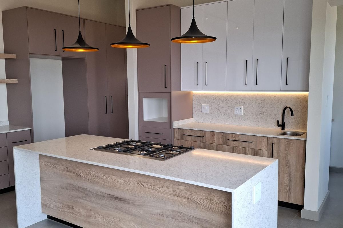 Modern kitchen featuring a central island with a gas hob, stone countertops, two-tone cabinetry, and integrated under-cabinet lighting.