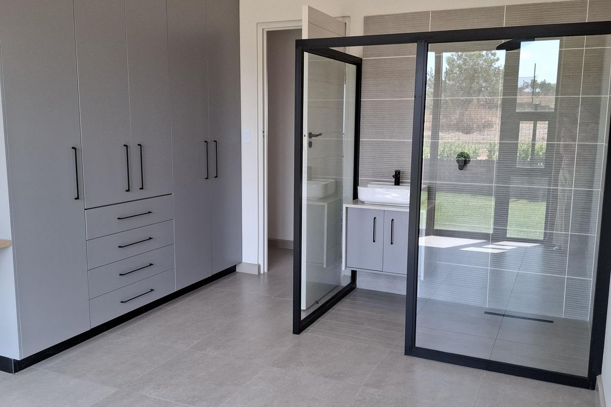 Modern bedroom featuring extensive built-in cabinetry and an open-plan en-suite bathroom with a glass-enclosed walk-in shower and vanity.