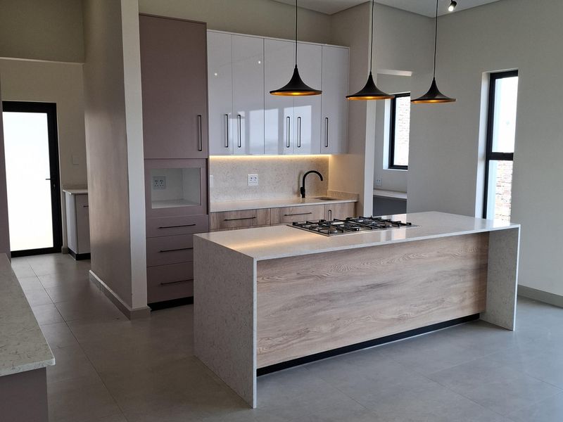 Modern kitchen featuring a central island with a gas hob, stone countertops, sleek cabinetry, and contemporary pendant lighting in an open-plan layout.