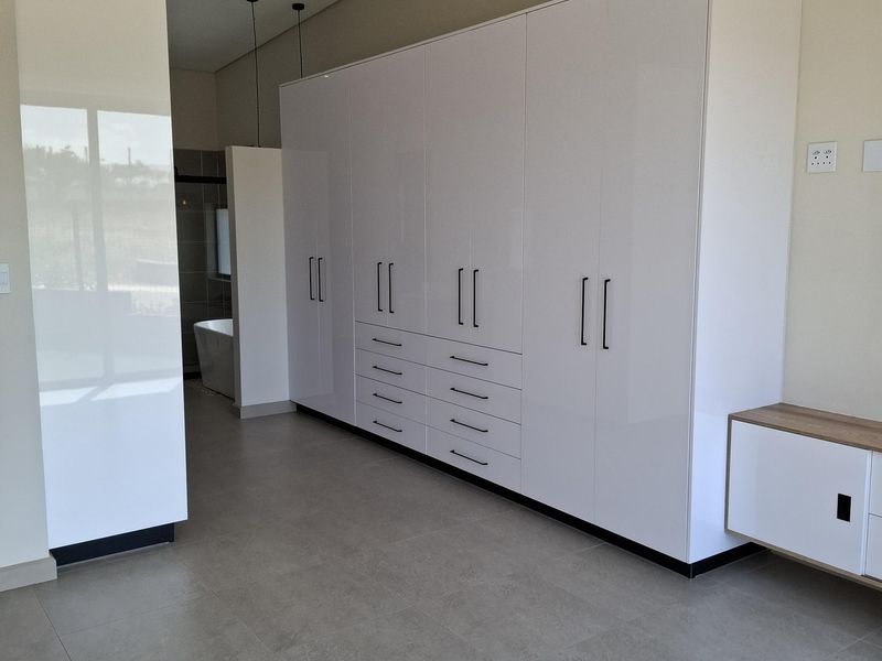 Spacious bedroom featuring extensive modern white built-in cupboards, large format floor tiles, and an integrated air conditioning unit.