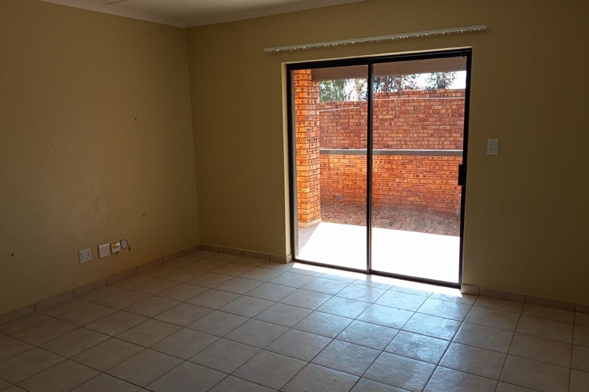 An empty living room featuring tiled flooring and a sliding glass door providing access to an outdoor patio area.