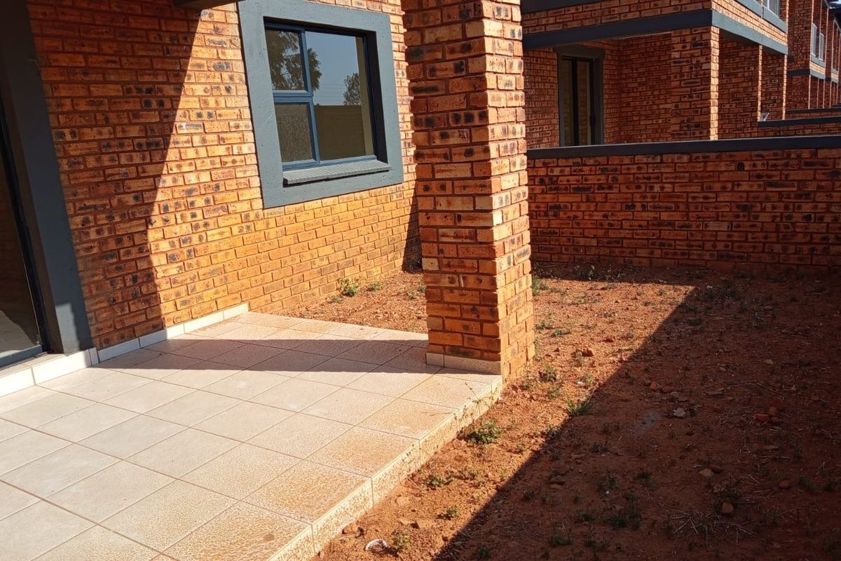 A ground floor apartment exterior featuring a tiled patio area and face brick facade, leading out to an unlandscaped garden space.