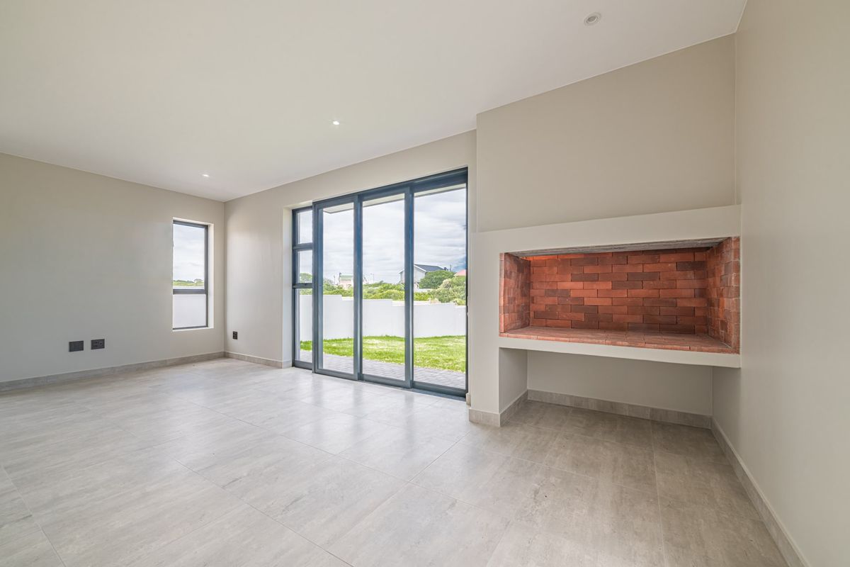 A bright, modern living area featuring large sliding glass doors, neutral tiled flooring, and a built-in brick fireplace, offering direct access to the garden.