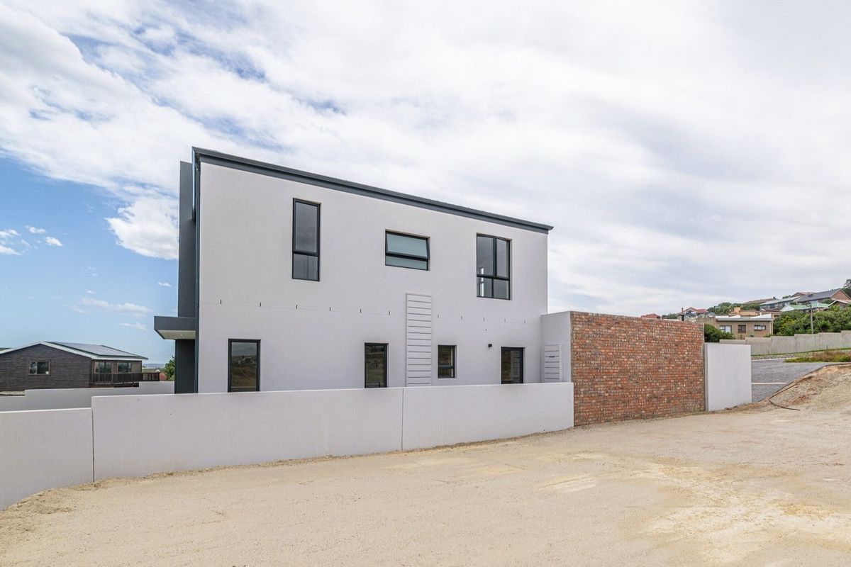 A modern two-story residential property featuring a clean plastered facade, contemporary window frames, and a combination of brick and plastered boundary walls.