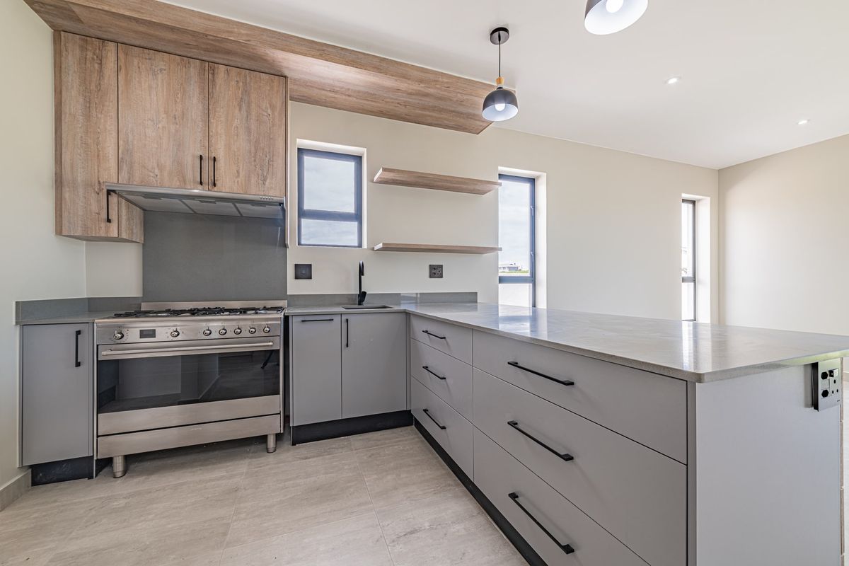 Modern kitchen featuring grey cabinetry, stone countertops, a gas stove with extractor, and floating shelves in an open-plan layout.