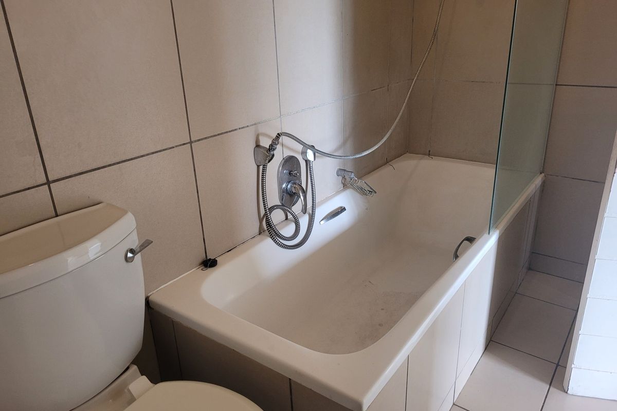 A functional bathroom featuring a bathtub with a shower mixer, glass screen, and neutral ceramic tiling throughout.