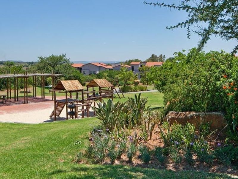 A well-maintained communal garden area featuring a children's playground, wooden pergola, and established landscaping within a residential apartment complex.