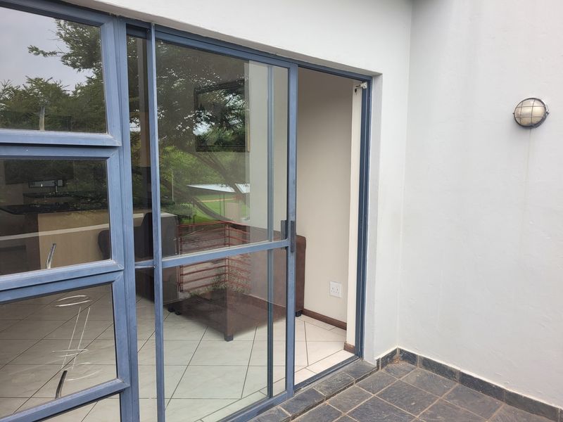 A covered patio area featuring tiled flooring, an exterior wall light, and a sliding glass door providing access to the interior living space.