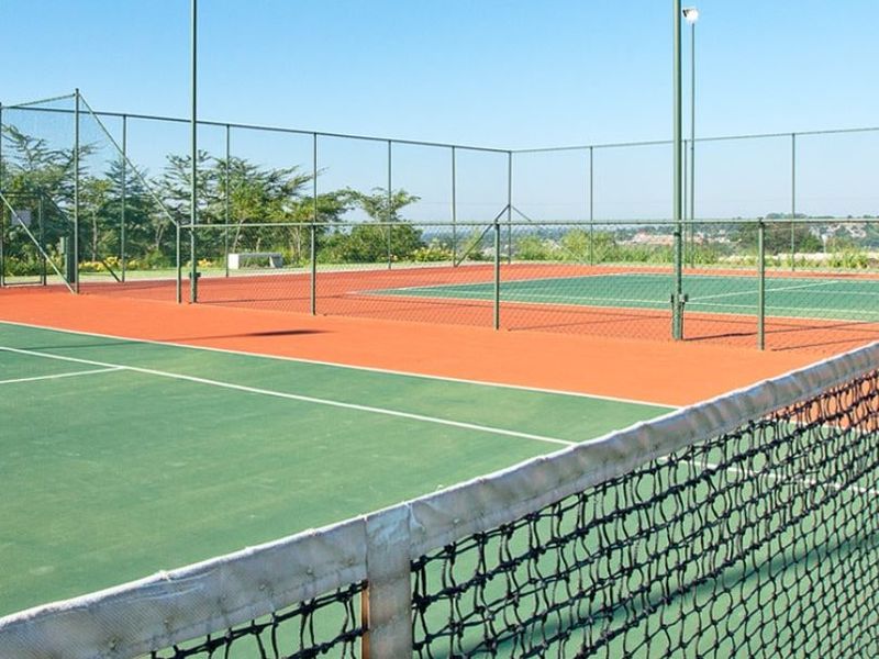 A well-maintained outdoor tennis court facility featuring durable surfacing, perimeter chain link fencing, and integrated floodlighting for evening play.