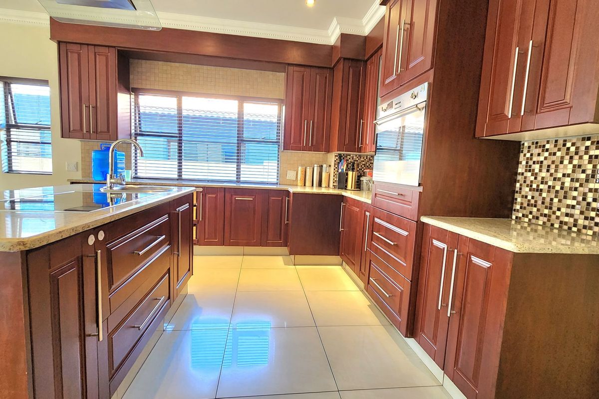 A well-maintained kitchen featuring dark wood cabinetry, granite countertops, a central island, and modern built-in appliances with a mosaic tile backsplash.