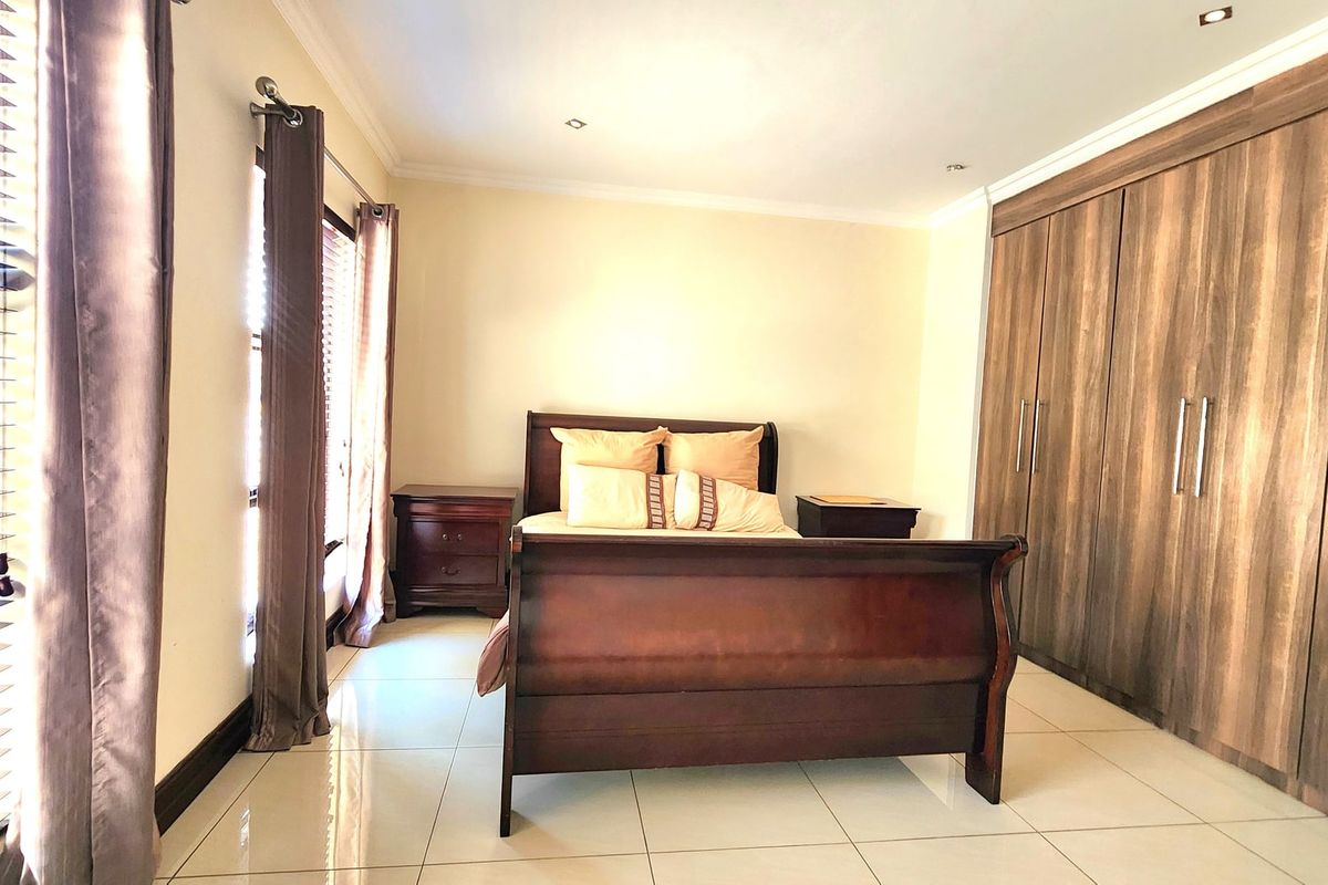 A well-maintained bedroom featuring large built-in wooden cupboards, neutral tiled flooring, and recessed ceiling lighting.