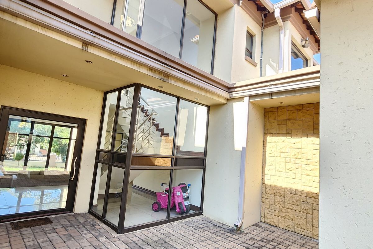 A paved rear courtyard featuring a stone-clad accent wall and a prominent glass-enclosed staircase structure with aluminium framing.