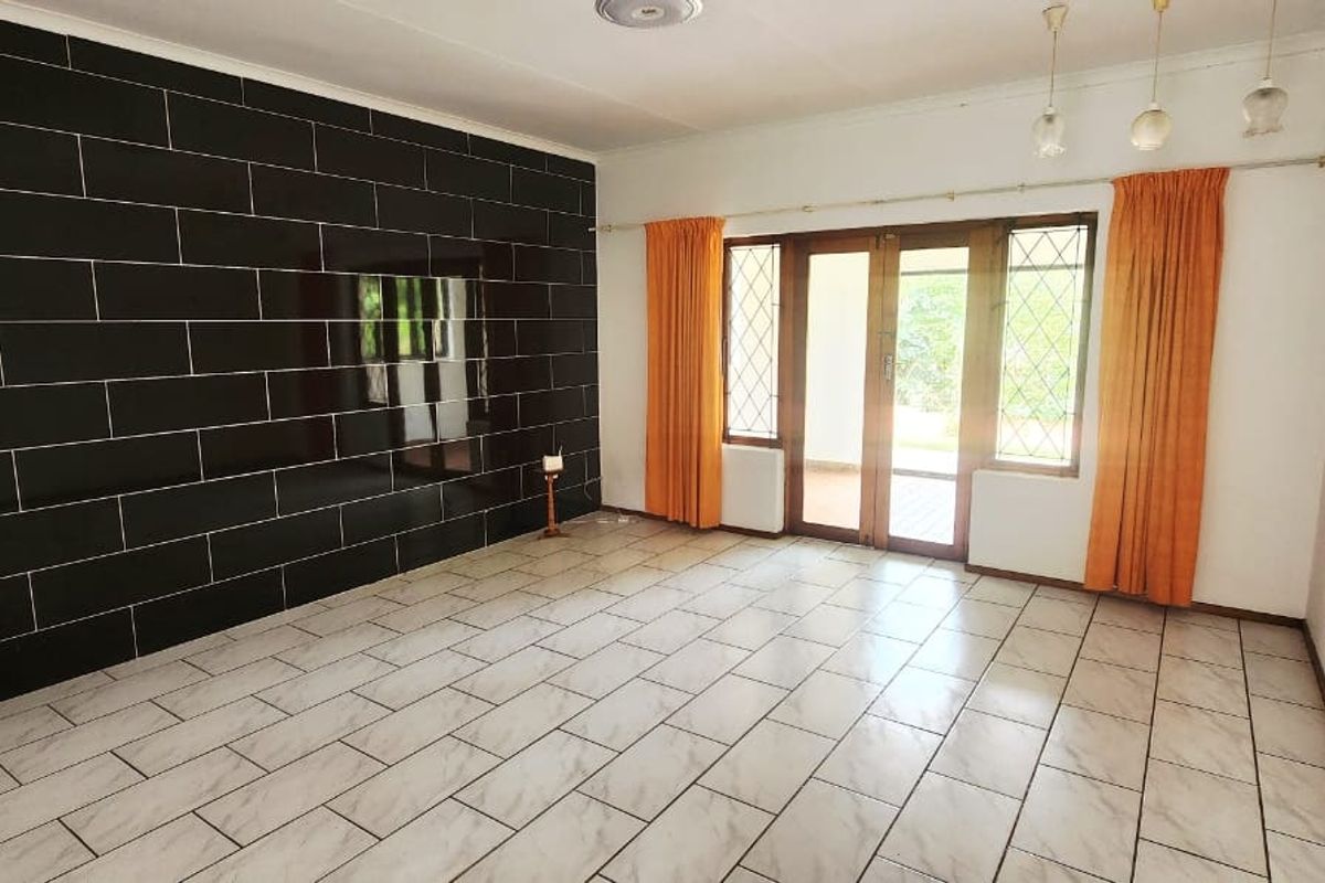Spacious living room featuring large format floor tiles, a striking black tiled feature wall, and access to the outdoor area through glass panelled doors.