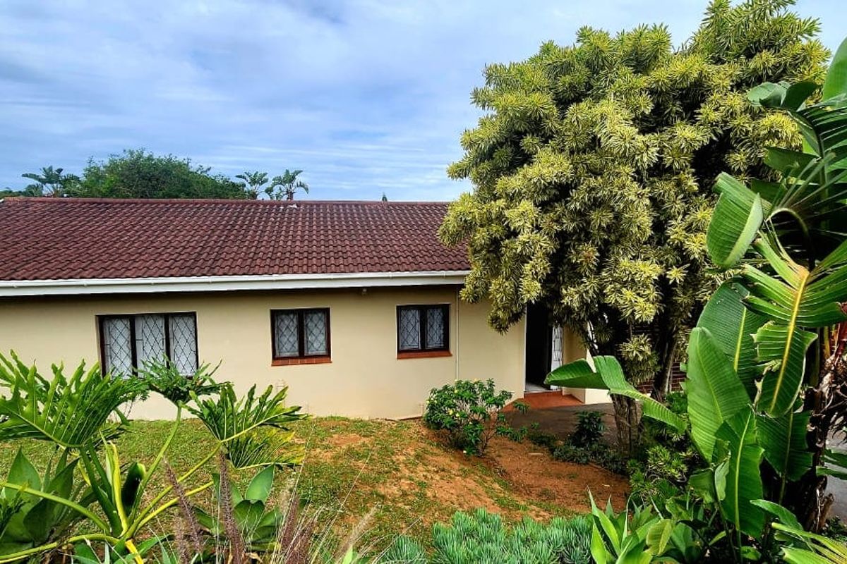 Rear view of the townhouse featuring a tiled roof, cream-colored exterior walls, and established garden landscaping.