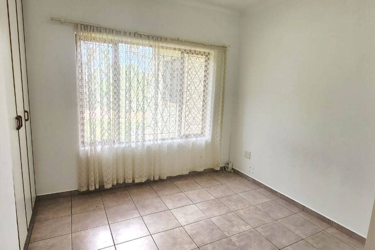 A vacant bedroom featuring tiled flooring and built-in cupboards, offering a clean and neutral space ready for personalization.