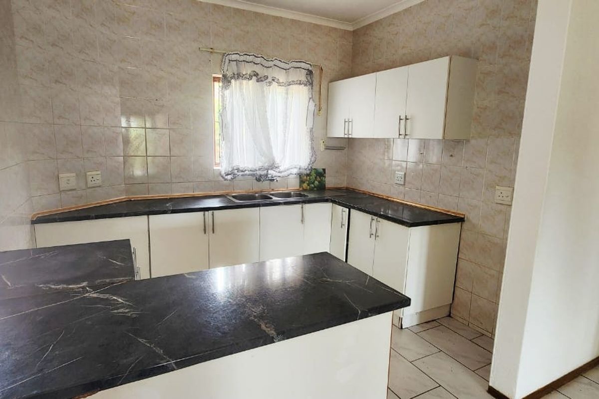 A functional kitchen featuring laminate countertops, a double basin sink, tiled backsplash, and ample built-in cabinetry, offering a clean and practical workspace.