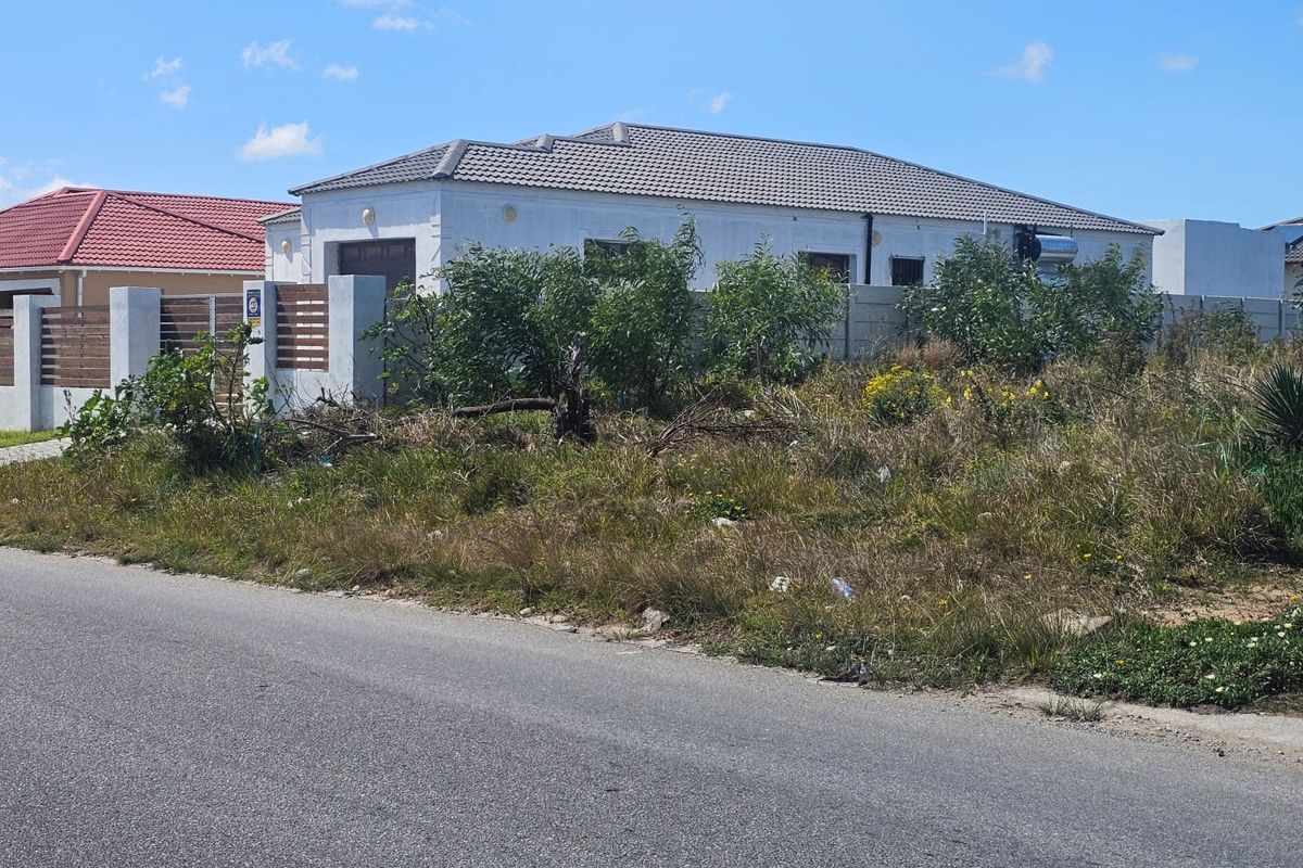A view of a residential property featuring a tiled roof home with a concrete boundary wall and an overgrown vacant plot in the foreground.