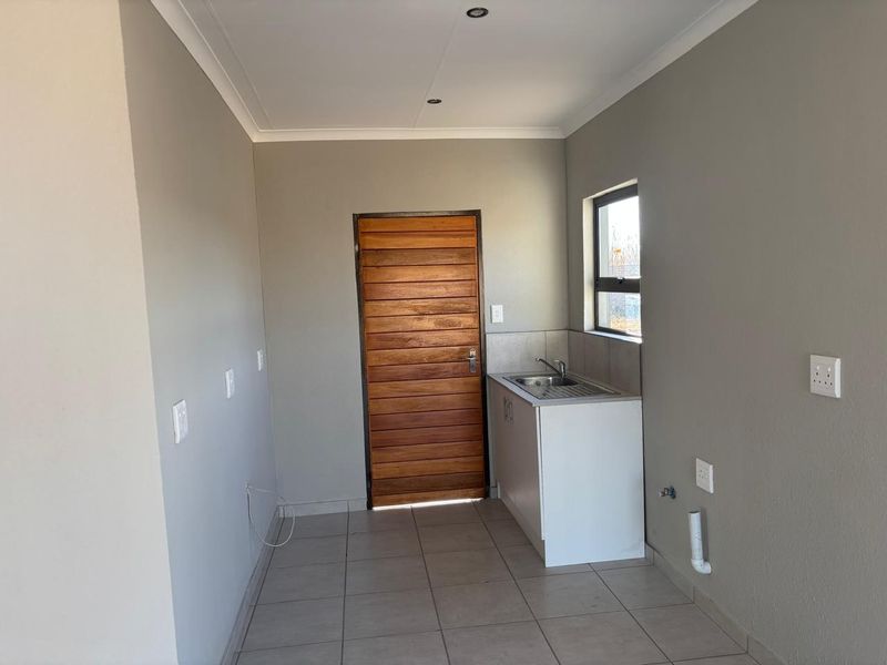 A clean, functional laundry area featuring tiled flooring, a stainless steel sink, and dedicated plumbing connections for appliances.